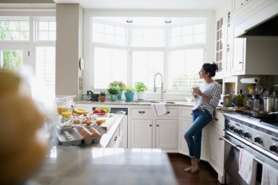 Pensive woman drinking coffee looking out window kitchen